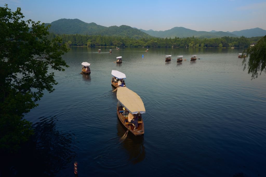 Calm lake scene with traditional boats sailing in Hangzhou under a clear sky.